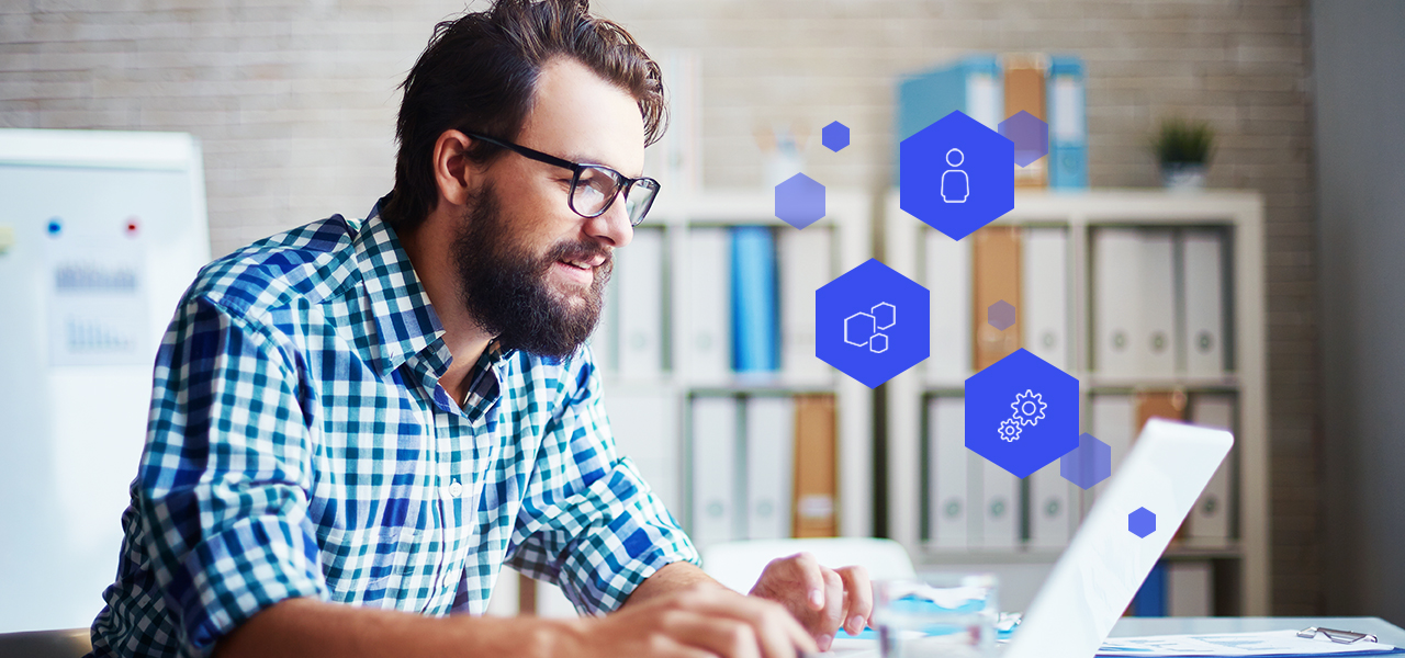 Man with glasses and plaid shirt working on a laptop in an office